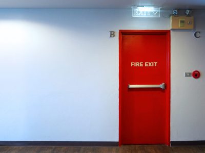 Fire exit emergency door red color metal material with alarm for safety protection and wood floor and white wall in building.